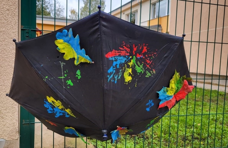 Ar izkrāsotām lapām rotāts lietussargs uz bērnudārza sētas