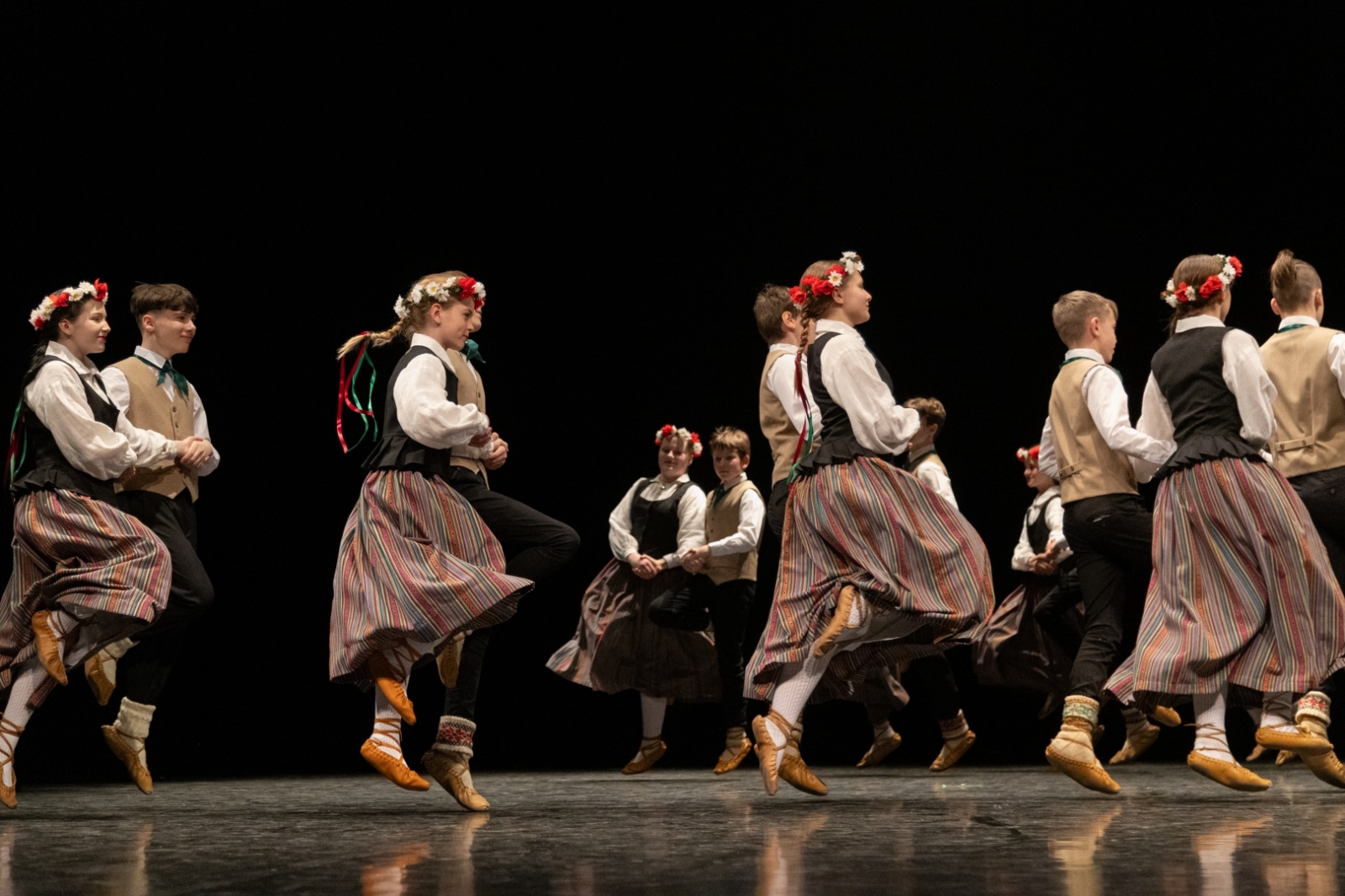Skolēnu tautas deju skates dalībnieki uz skatuves tautas tērpos