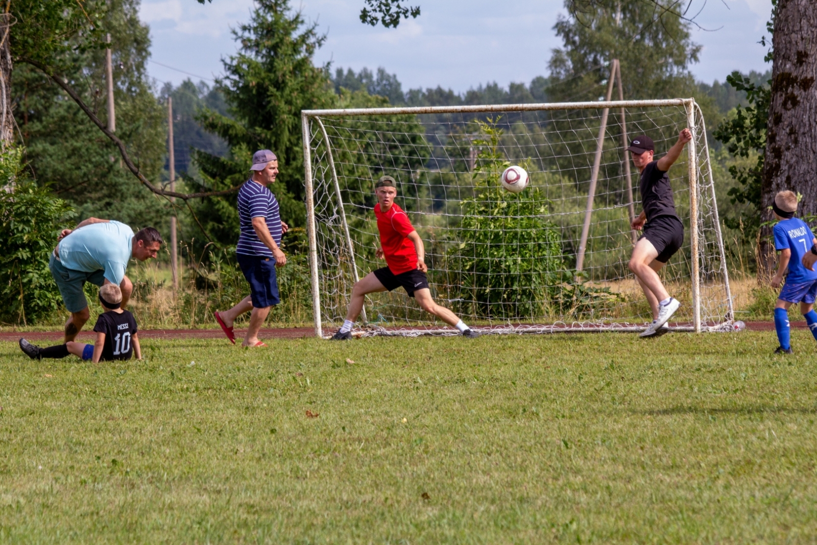 Vīrieši spēlē futbolu, puisis sarkanā kreklā vārtos Taurupes pagasta svētkos 07.2024.